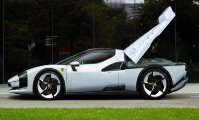 White sports car with open gull-wing door parked on grass.