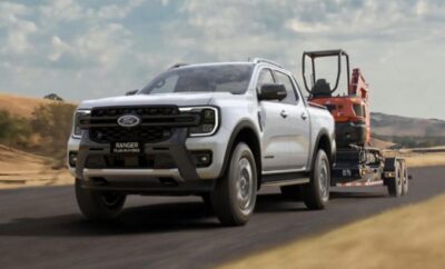 White Ford pickup truck towing a red tractor on a trailer.