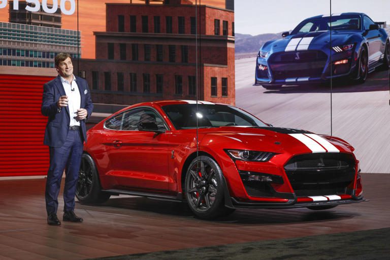 A man presenting a red sports car on stage at an event.