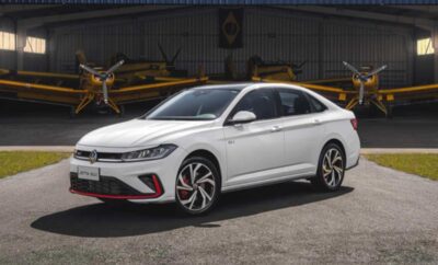 A white sporty hatchback parked outdoors near industrial equipment.