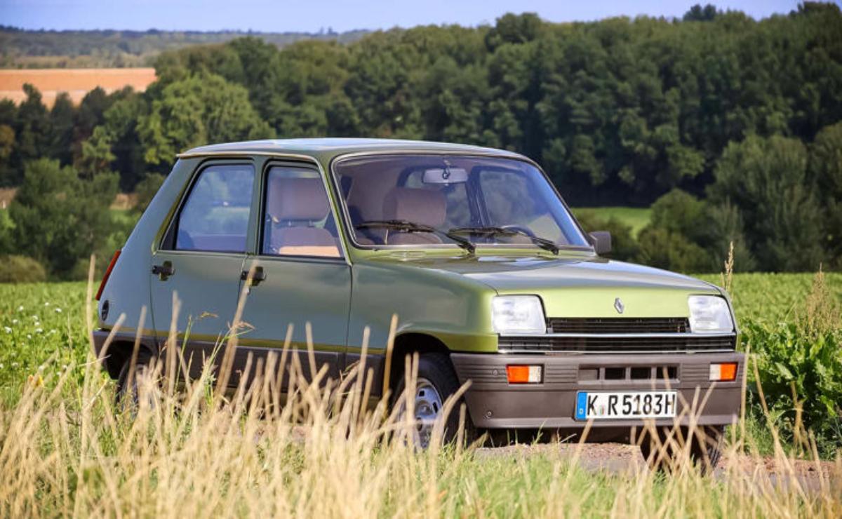 A classic green Renault 5 parked in a grassy field with trees in the background.