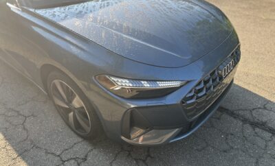 Close-up of a sleek gray car's front hood and headlight in sunlight.