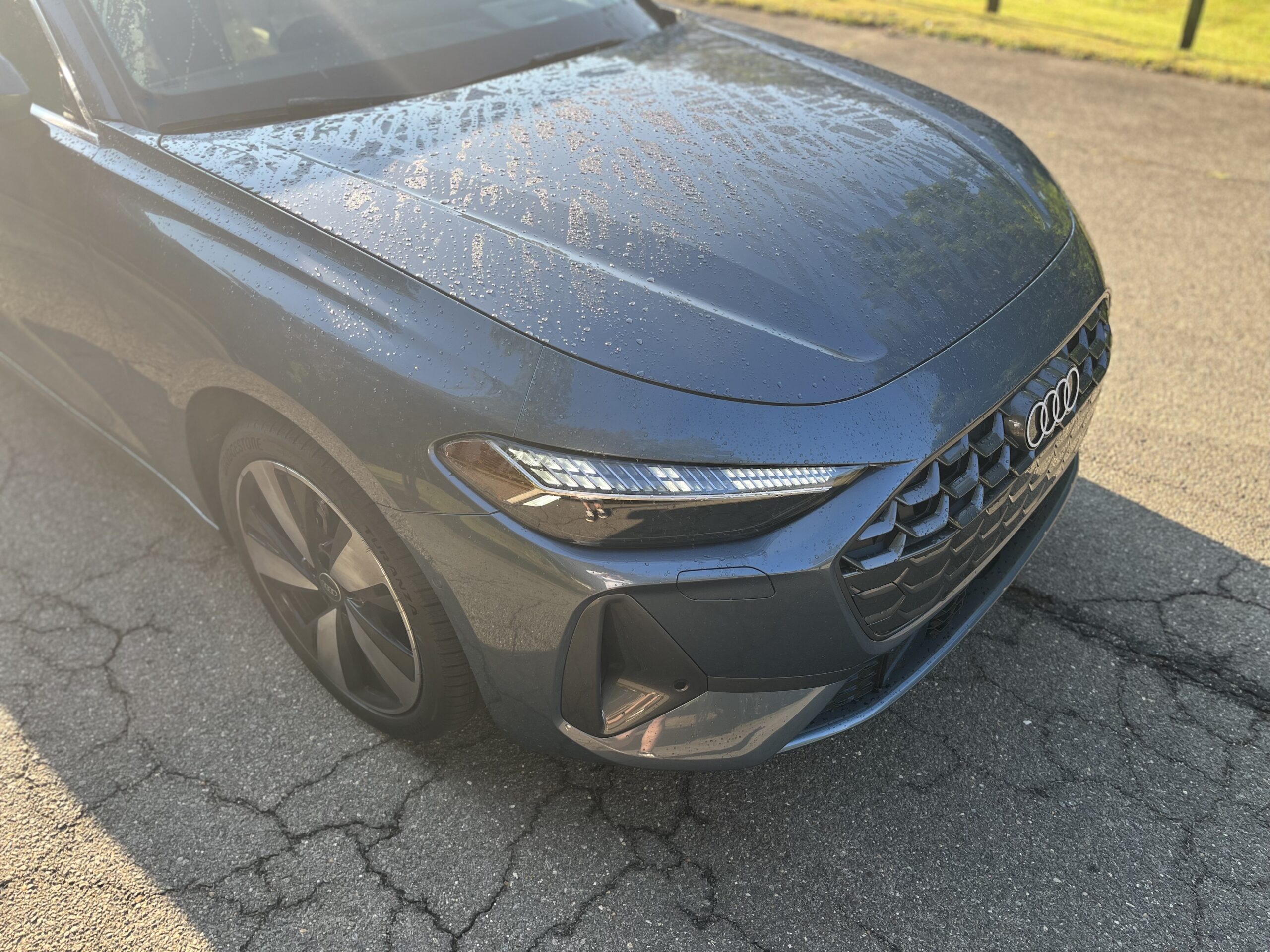Close-up of a sleek gray car's front hood and headlight in sunlight.