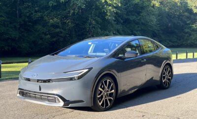 A sleek silver electric car parked on a sunny road with greenery in the background.