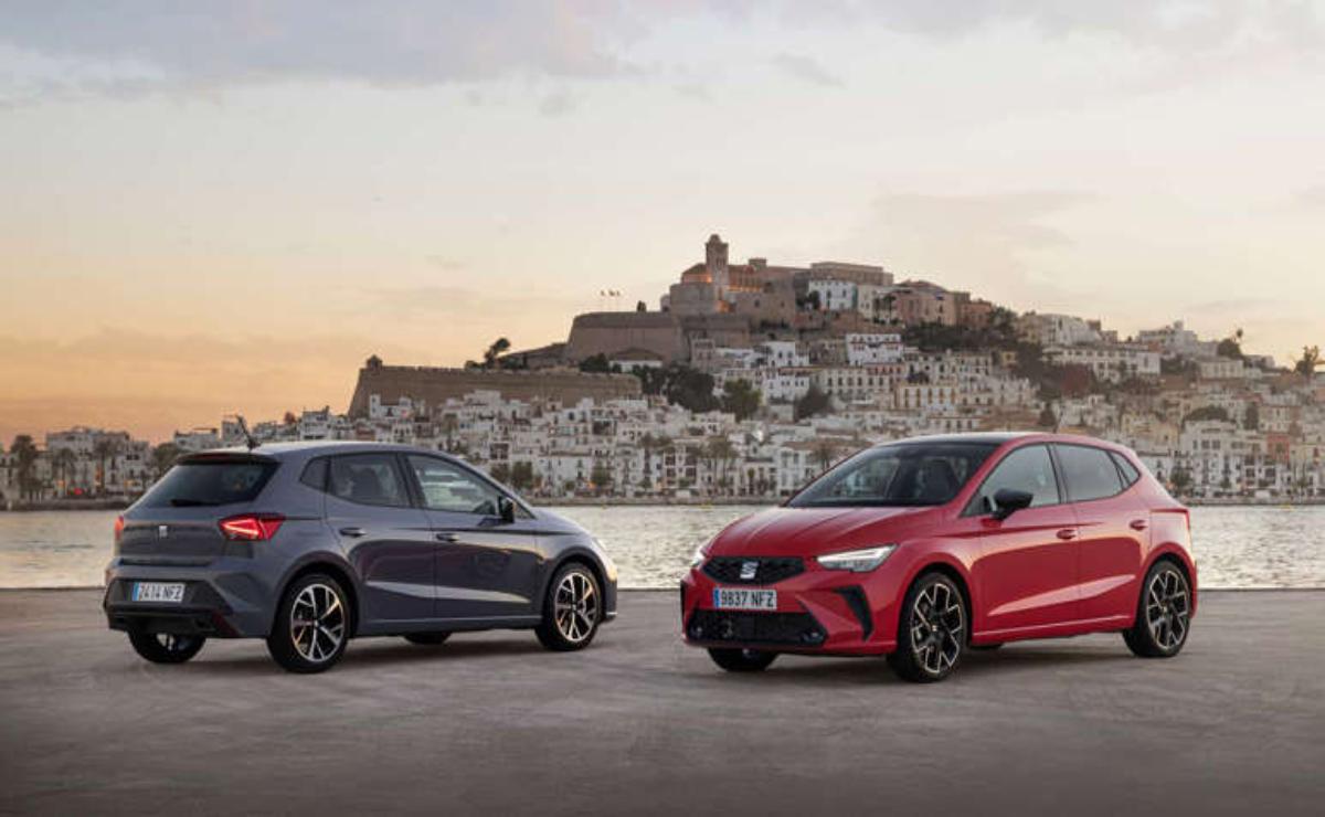 Two sporty cars parked with a historic hilltop town at sunset.