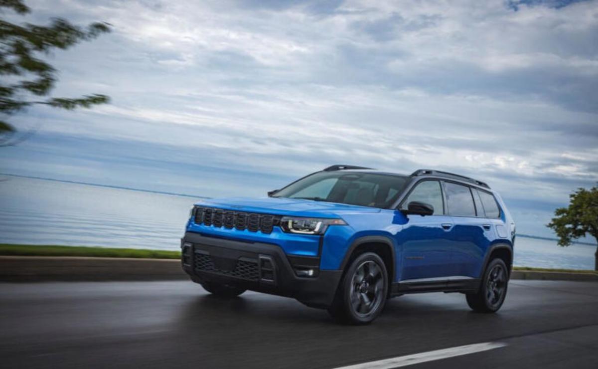 Blue SUV driving on a coastal road under a cloudy sky.