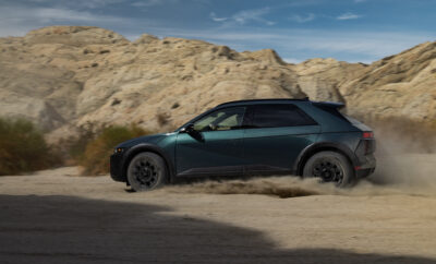 A sleek dark green compact car parked on a sandy terrain with rocky hills.