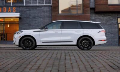 White luxury SUV parked on cobblestone street beside modern building.