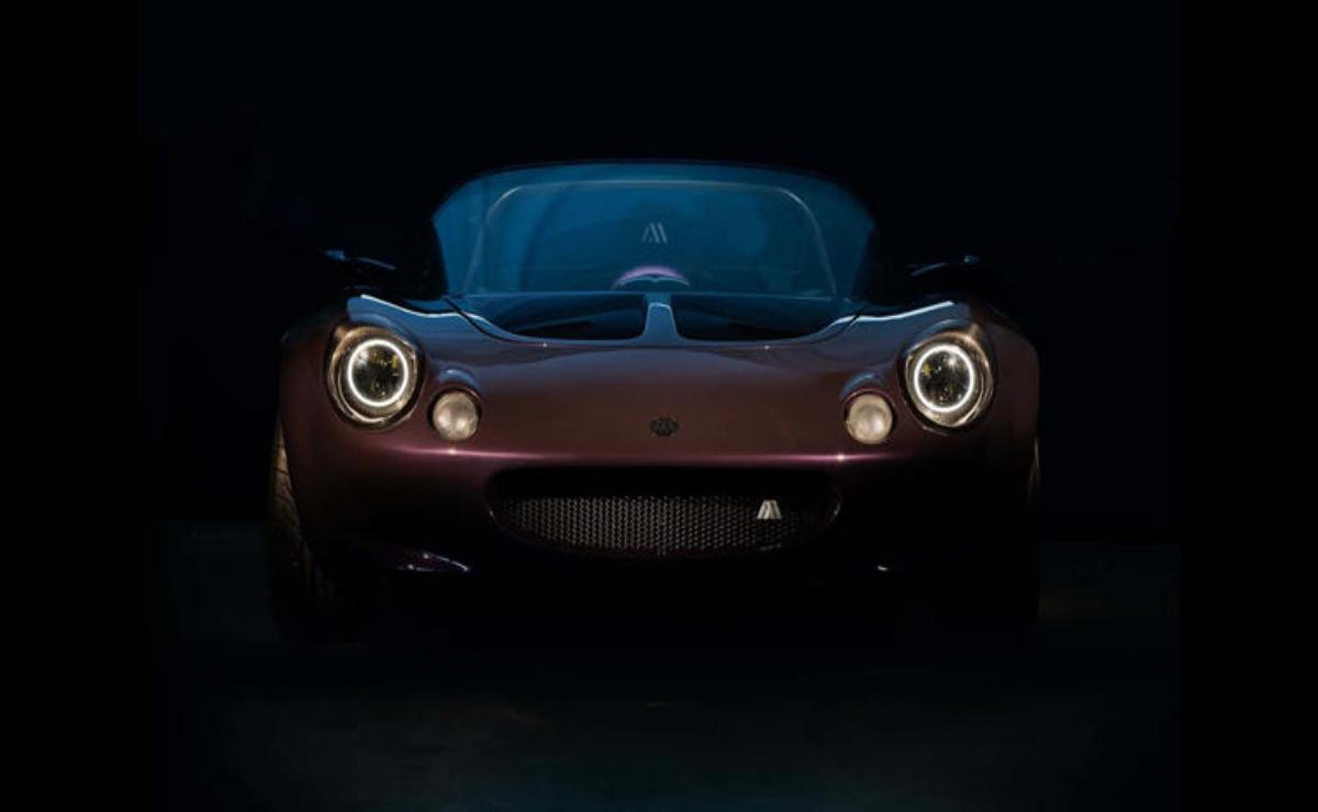 Dark, sleek sports car illuminated by headlights in a black background.