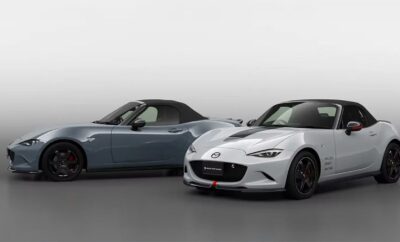 Two Mazda MX-5 Miata sports cars, one blue and one white, side by side in a studio.