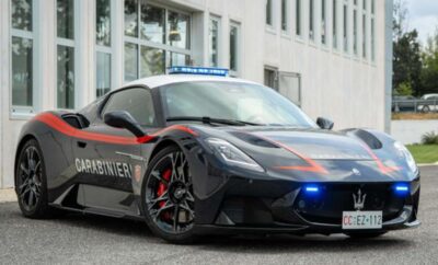 A sleek black police car with flashing blue lights parked by a building.