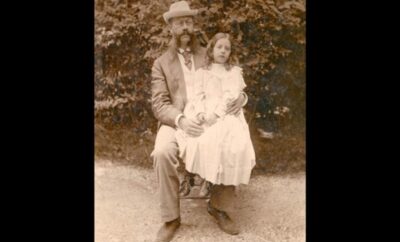 A vintage photo of a man and girl sitting together outdoors.