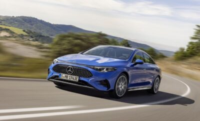 A blue Mercedes-Benz coupe driving on a scenic road.