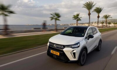 White SUV driving along a coastal road with palm trees and the sea in the background.