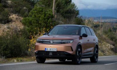 A sleek, modern copper-colored SUV driving on a road with greenery and mountains in the background.