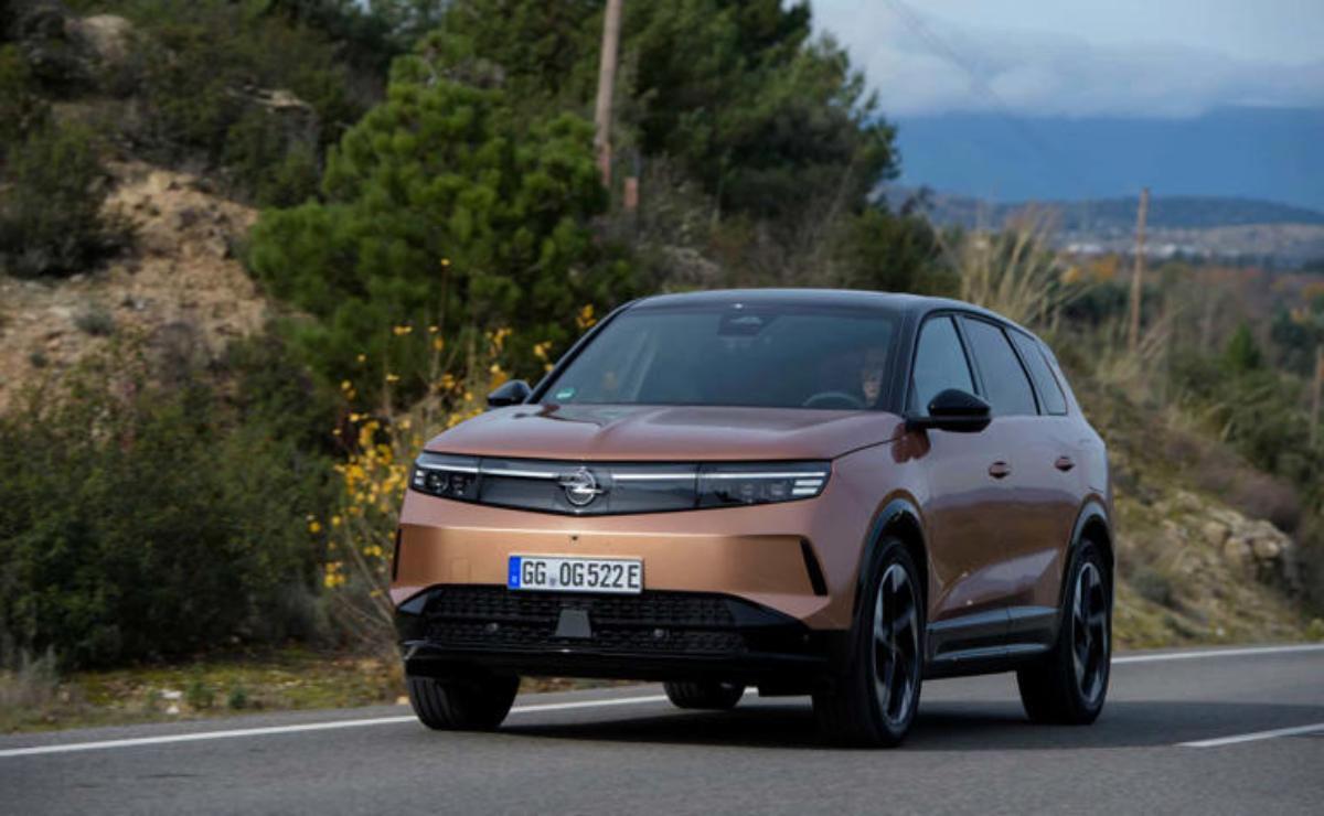 A sleek, modern copper-colored SUV driving on a road with greenery and mountains in the background.