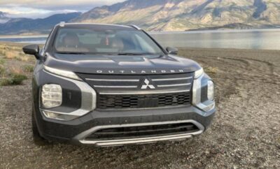 Black Mitsubishi SUV parked near a lake with mountains in the background.