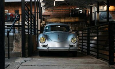 Classic silver car parked inside a rustic garage with wooden beams.