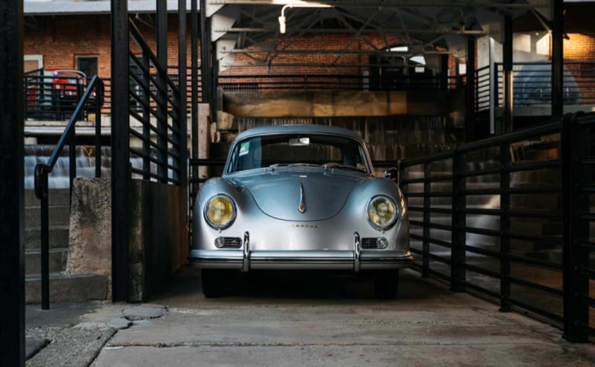 Classic silver car parked inside a rustic garage with wooden beams.