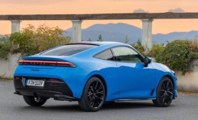 Sleek blue sports car parked with a scenic bridge and mountain backdrop.