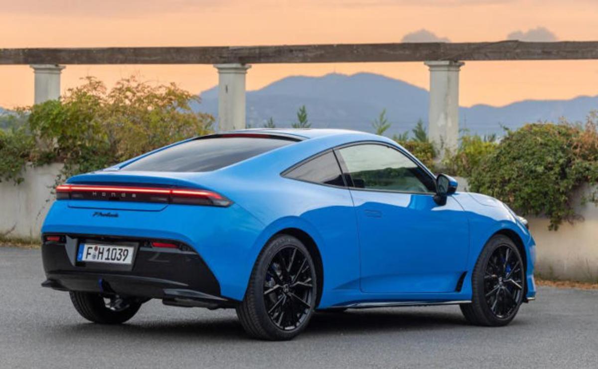 Sleek blue sports car parked with a scenic bridge and mountain backdrop.