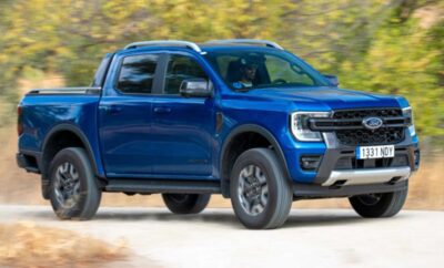 Blue pickup truck driving on a road with trees in the background.