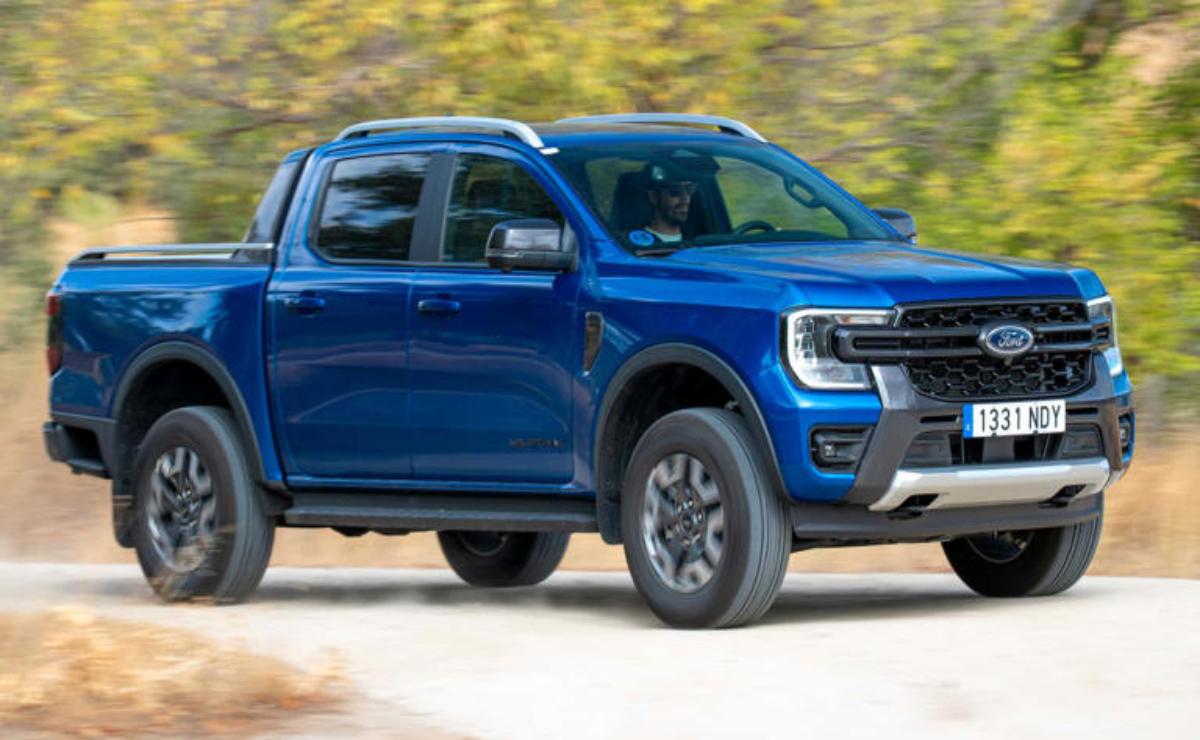 Blue pickup truck driving on a road with trees in the background.