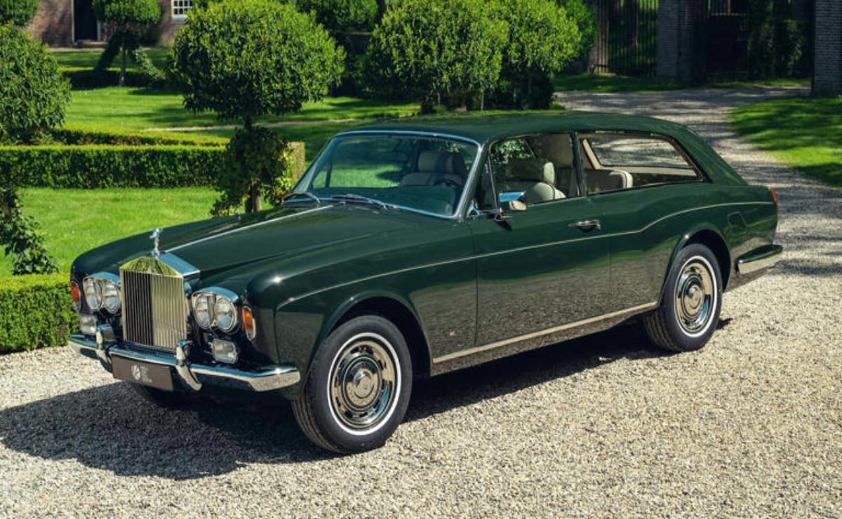 Classic green convertible car parked on a gravel driveway surrounded by greenery.