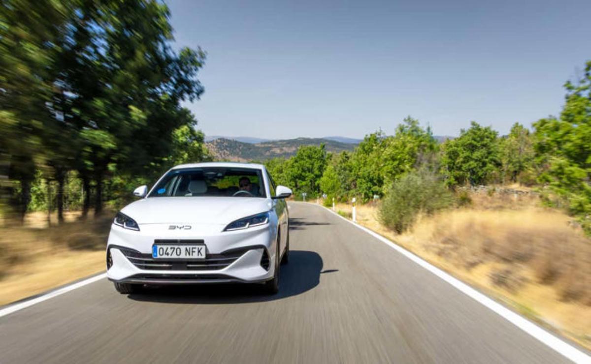 A white electric car driving on a sunny country road.