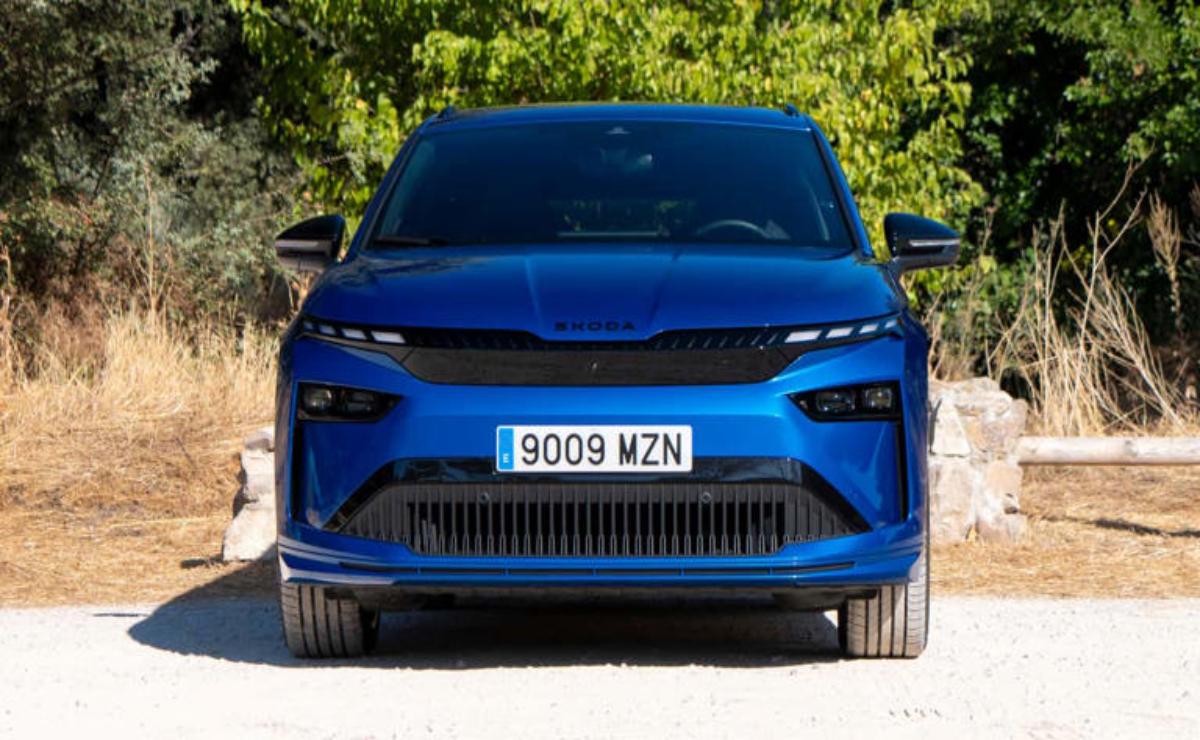 Blue electric SUV parked on a dirt road with trees in the background.