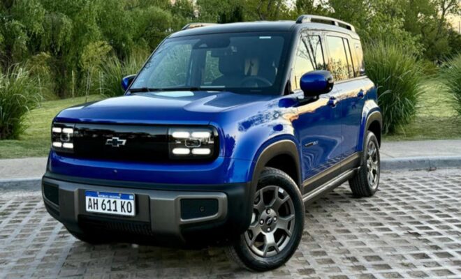 Blue compact SUV parked on a stone driveway with greenery in the background.