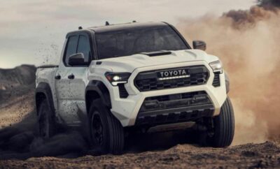 White Toyota pickup truck driving off-road on dirt terrain.
