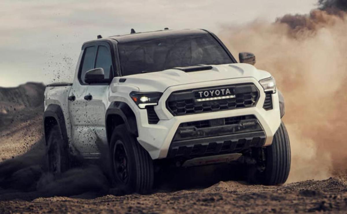 White Toyota pickup truck driving off-road on dirt terrain.