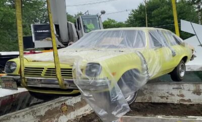 A yellow vintage car wrapped in plastic on a trailer.