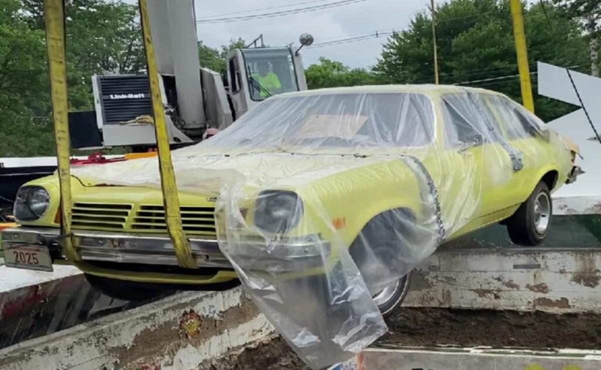 A yellow vintage car wrapped in plastic on a trailer.