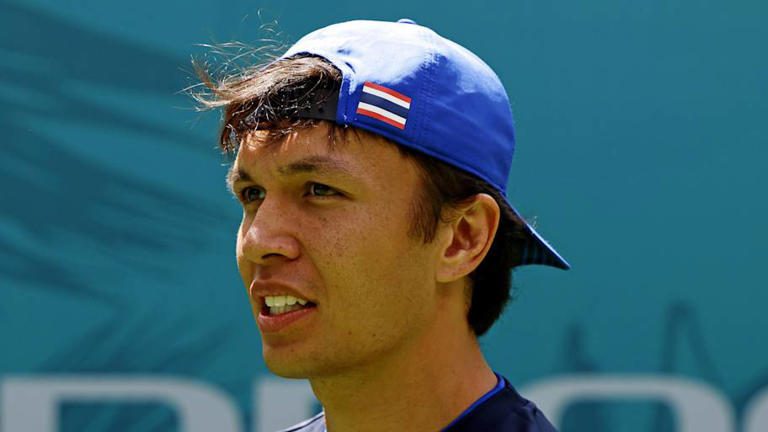 Young man wearing a blue baseball cap backward outdoors.