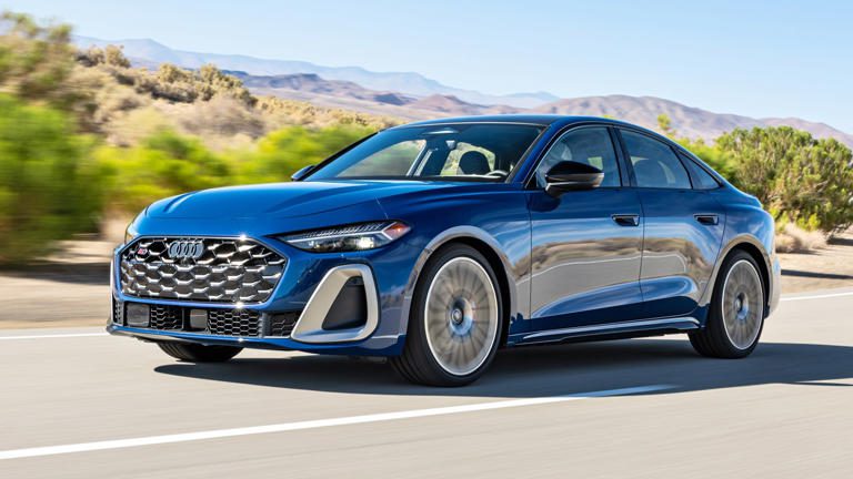 Sleek blue luxury sedan driving on an open road with mountains in the background.