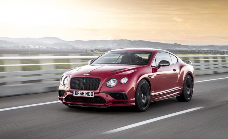 A sleek red luxury sports car driving on a highway.
