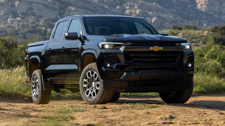 Black Chevrolet pickup truck parked on rugged terrain with mountains in the background.