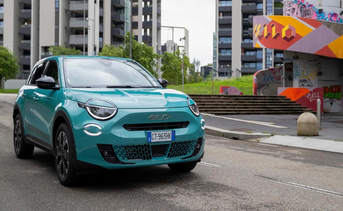 A teal Fiat 500 parked on a city street near modern apartment buildings.
