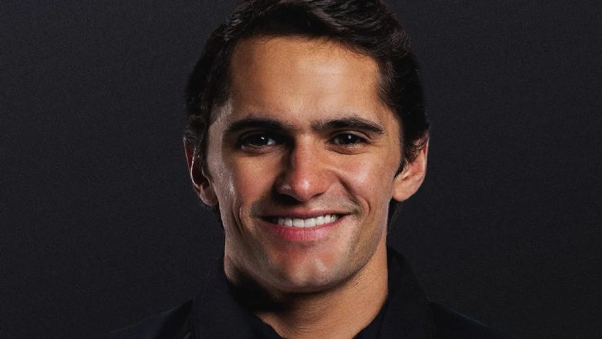 Portrait of a smiling young man with dark hair against a dark background.