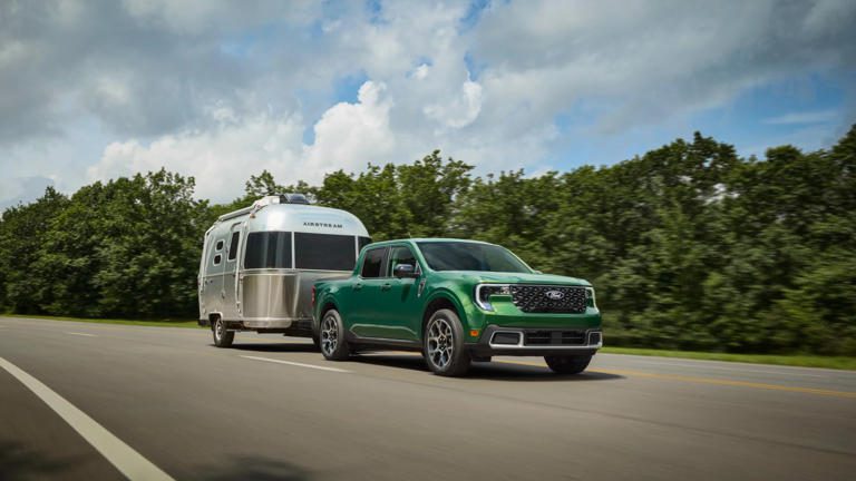 Green pickup truck towing a silver camper trailer on a road.