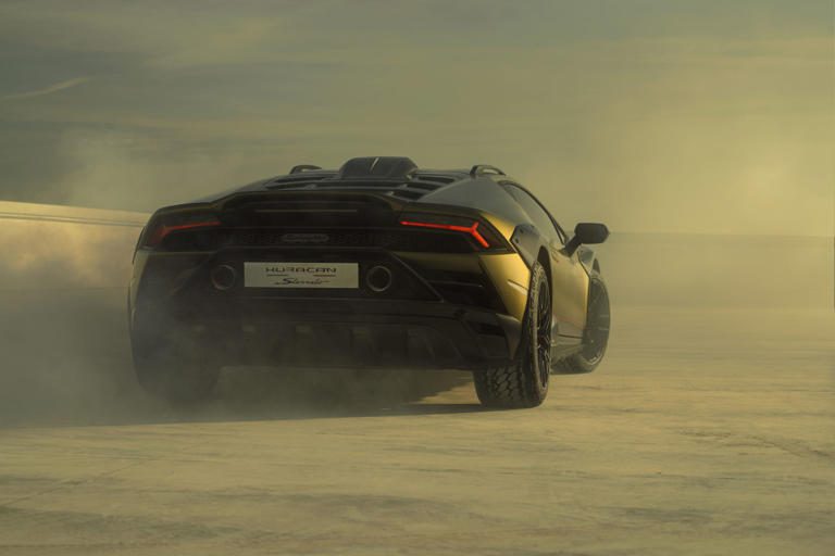 A sleek black sports car speeding on a dusty road at sunset.