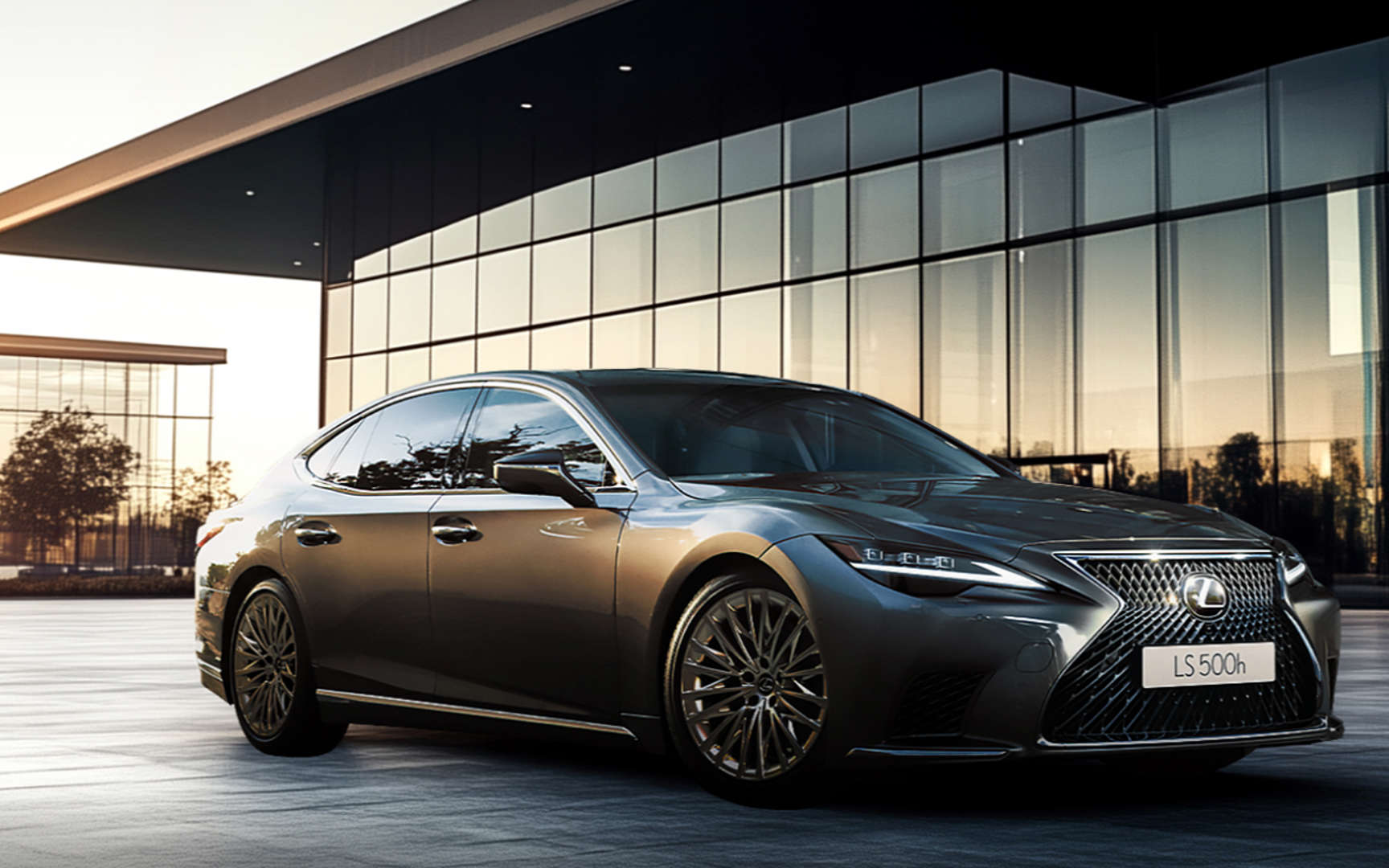 Sleek black luxury sedan parked by a modern glass building at sunset.