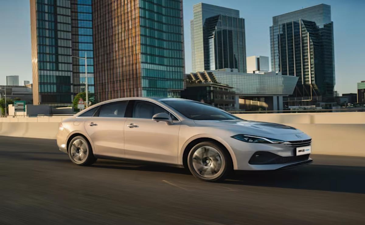A sleek silver sedan driving through a modern cityscape at sunset.