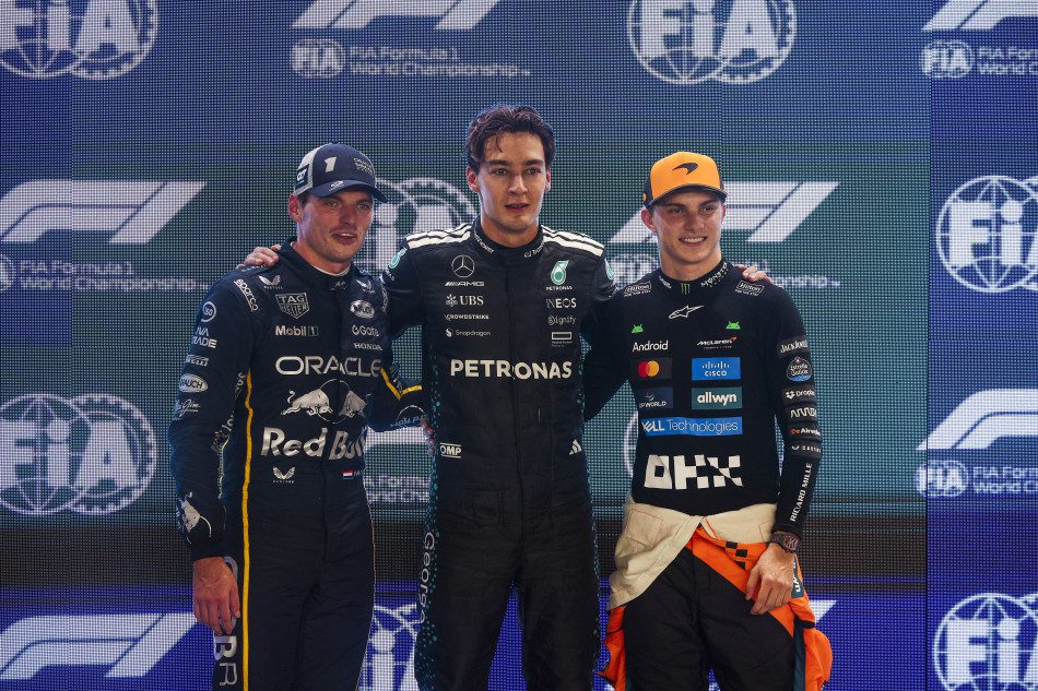 Three F1 drivers posing together on the podium after a race.