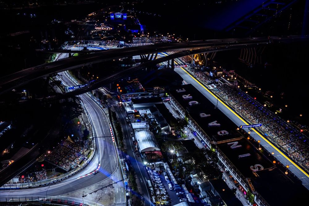 Aerial night view of a brightly lit NASCAR race track with cars racing.