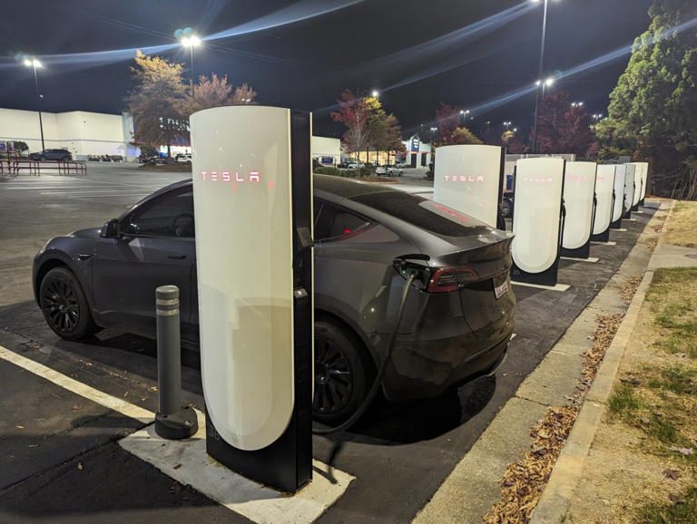 Tesla car charging at a Supercharger station at night.
