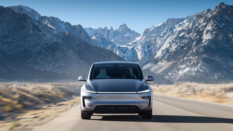 A sleek electric SUV driving on a mountain road with snowy peaks.