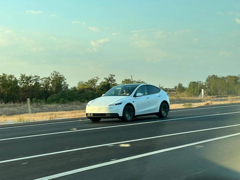 White Tesla Model Y driving on an open road during daytime.